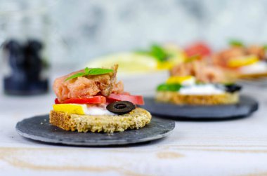 Hafif ahşap zemin üzerinde pembe somon balığı, salatalık, domates, zeytin ve limon bulunan küçük bir kanepe.