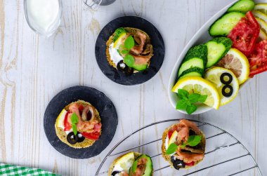 Hafif ahşap zemin üzerinde pembe somon balığı, salatalık, domates, zeytin ve limon bulunan küçük bir kanepe.