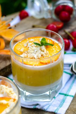 Beyaz ve turuncu katmanlı iki galon şeftalili panna cotta. Nane ve kirazlı ahşap arka planda servis edilir..