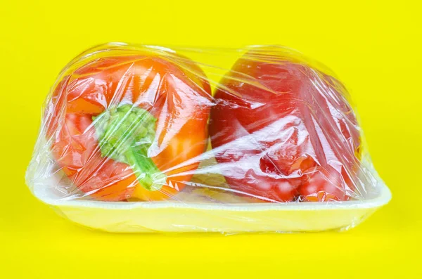 Fresh food in plastic package recycling and environment eco problem concept. Bell pepper wrapped in plastic on yellow background