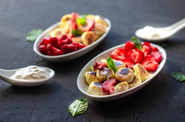 Siyah arka planda bal ve çilekli mini peynir krepleri. Düzgün beslenme sağlıklı tatlı