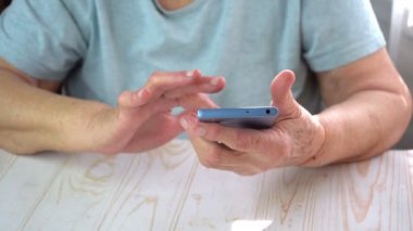 Yaşlı kadın dokunmatik ekranlı akıllı telefon kullanmaya çalışıyor, yaşlı kadının elleri telefon ekranını kaydırıyor.