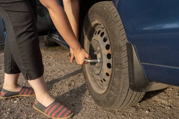 woman tighten the bolts on a disk, changing tire manually, car wheel