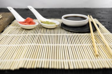 Japon mutfak arka planında bambu hasırı, yemek çubuğu, siyah arka planda soya sosu.