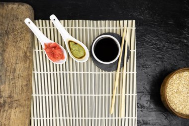 Japon mutfak arka planında bambu hasırı, yemek çubuğu, siyah arka planda soya sosu.