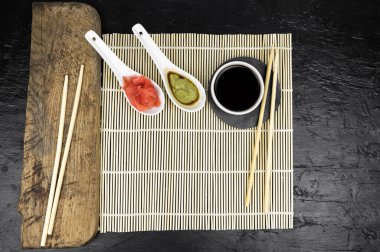 Japon mutfak arka planında bambu hasırı, yemek çubuğu, siyah arka planda soya sosu.