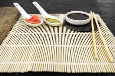 Japon mutfak arka planında bambu hasırı, yemek çubuğu, siyah arka planda soya sosu.
