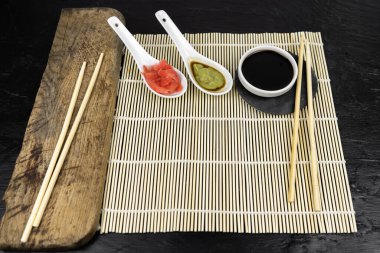 Japon mutfak arka planında bambu hasırı, yemek çubuğu, siyah arka planda soya sosu.