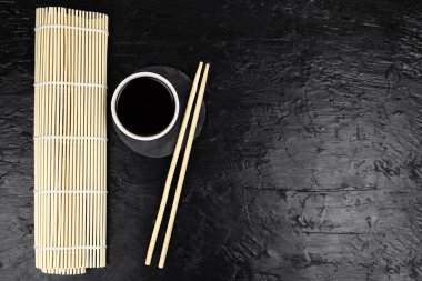 Japon mutfak arka planında bambu hasırı, yemek çubuğu, siyah arka planda soya sosu.