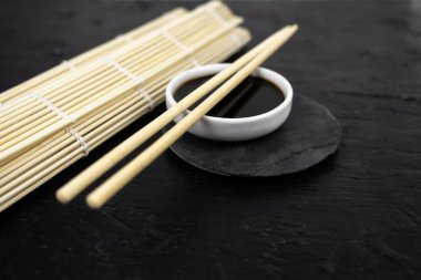 Japon mutfak arka planında bambu hasırı, yemek çubuğu, siyah arka planda soya sosu.