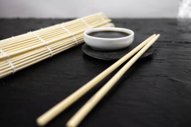 Japon mutfak arka planında bambu hasırı, yemek çubuğu, siyah arka planda soya sosu.