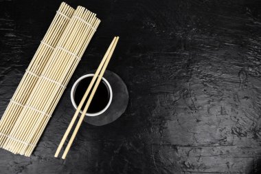 Japon mutfak arka planında bambu hasırı, yemek çubuğu, siyah arka planda soya sosu.