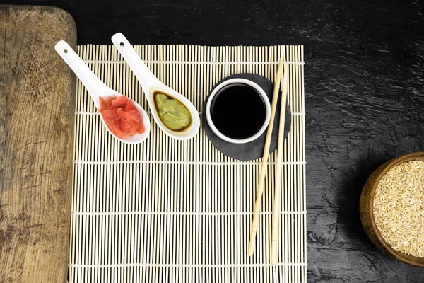Japon mutfak arka planında bambu hasırı, yemek çubuğu, siyah arka planda soya sosu.