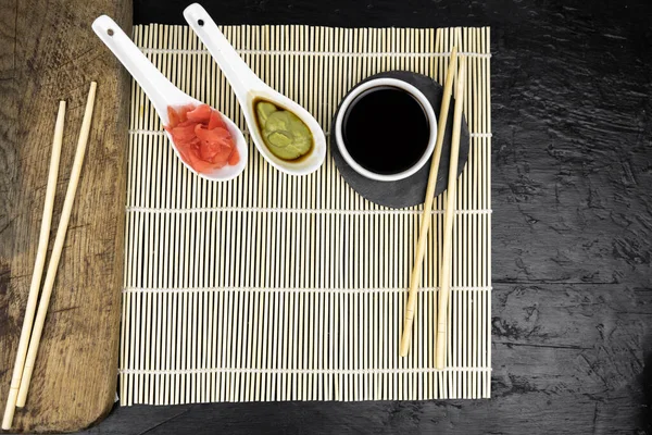 Japanese kitchen background with bamboo mat, chopsticks, soy sauce on black background