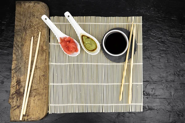 Japon mutfak arka planında bambu hasırı, yemek çubuğu, siyah arka planda soya sosu.