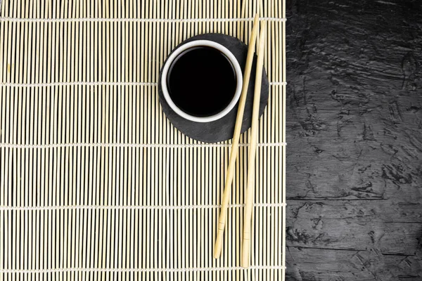 Japanese kitchen background with bamboo mat, chopsticks, soy sauce on black background