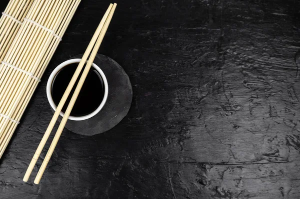 Japanese kitchen background with bamboo mat, chopsticks, soy sauce on black background