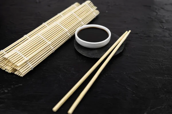 Japon mutfak arka planında bambu hasırı, yemek çubuğu, siyah arka planda soya sosu.