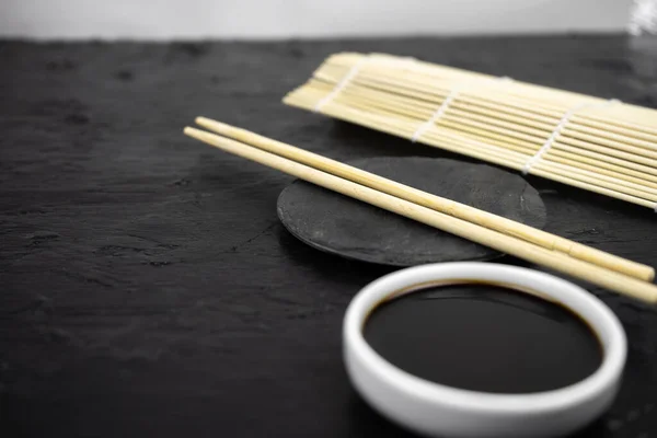 Japanese kitchen background with bamboo mat, chopsticks, soy sauce on black background