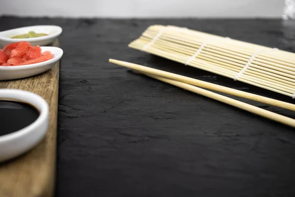 Japanese kitchen background with bamboo mat, chopsticks, soy sauce on black background