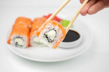 Bir Philadelphia maki rulosu al ve soya sosunun içine koy. Pembe zencefil, beyaz tabakta wasabi, Asya yemeği, Japon mutfağı geçmişi.