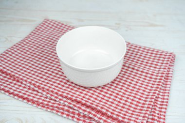 Kırmızı bir mutfak havlusunda beyaz, boş seramik kase..