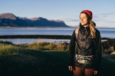 Uzun saçlı ve ince tebessümlü bir kız İzlanda sahilinde gün batımına hayran. Arka plan Atlantik Okyanusu 'nu ve dağların zirvelerini gösteriyor..