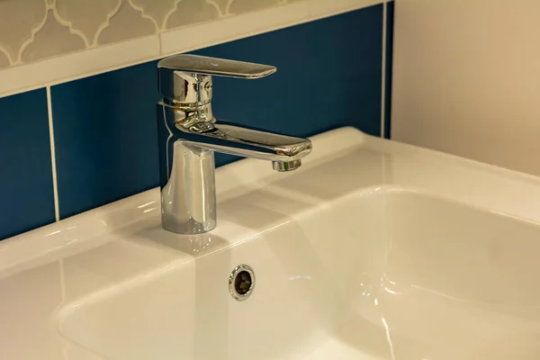 Photo of the interior of the bathroom. Chrome modern tap and ceramic white sink. Close-up, modern design. The concept of cleanliness.