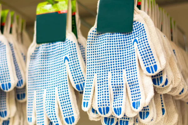 Garden gloves with a blue protective layer. A lot of white fabric gloves hung on the shelves. Protection of hands from dirt and scratches.
