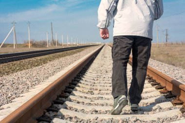 Demiryolu rayları kapanıyor. Bir adam rayları ileri doğru gider. Açık yol kavramı, geçmişi bırak, yeni bir hayata başla.