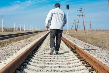 Bir adam demiryolu rayları boyunca yürür baharda mavi gökyüzünün arka planına karşı. Onun için yeşil bir trafik ışığı yanıyor. Özgürlük kavramı, geçmişten uzaklaş, yolu aç. 