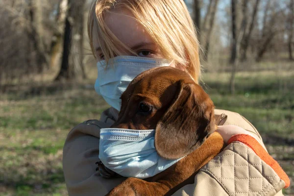 Tıbbi maskeli genç bir kız tıbbi maske takan bir köpeği tutuyor. İnsanlar ve evcil hayvanlar için Coronavirus koruması. COVID-19 köpek için tehlikeli..