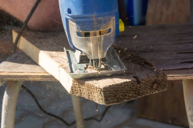 Bir adam elektrikli testereyle eski bir tahtayı kesiyor. Eylem halindeki bir yapbozun yakın çekimi.