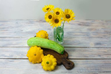 Ahşap masada yeşil kabak ve sarı mini köfte tava kabağı. Cam vazoda güzel sarı çiçekler.