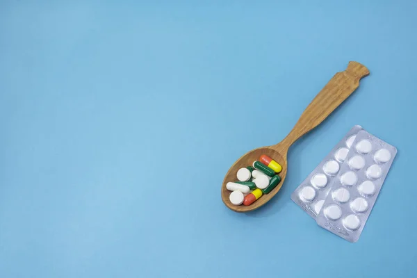 Tablets and capsules with vitamins in wooden spoon on blue background. Copy space, selective focus. The concept of medication, medicine, pharmaceuticals.