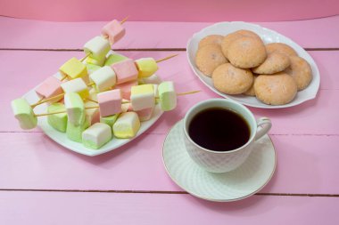 Bir fincan sade kahve, marşmelov ve ev yapımı kurabiyeler. Pembe ahşap arka plan. Kahve molası.