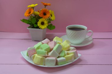 Beyaz tepside farklı meyvelerden gelen şekerlemeler. Pembe ahşap masada bir fincan koyu kahve. Kahve zamanı, romantik ruh hali..