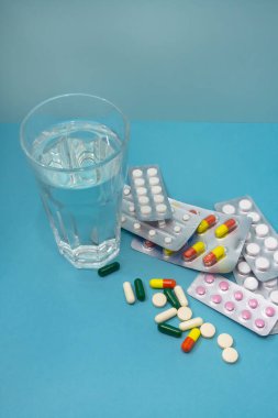 Mavi arka planda su toplayan bir sürü ilaç var. İlaç için bir bardak temiz su. Bir virüse ve sağlığa karşı tedavi kavramı.