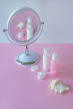 Aynada yansıması olan kozmetik ürünleri için şişe ve kap. Marka modeli için boş etiket. Pembe masa, pastel renkler. Cilt bakımı kavramı için doğal kozmetik ürünleri.