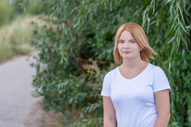 Beyaz elbiseli mutlu sarışın bir kadının portresi. Yazın parkta yürürken arka plan bulanıktı..