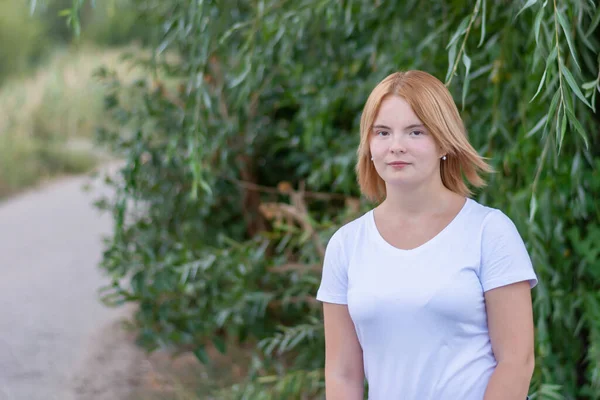 Beyaz elbiseli mutlu sarışın bir kadının portresi. Yazın parkta yürürken arka plan bulanıktı..