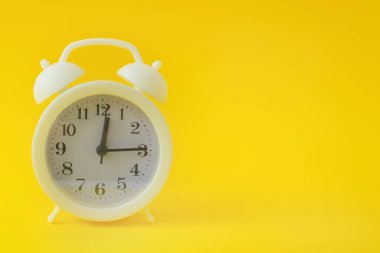 Parlak sarı bir zemin üzerinde beyaz antika çalar saat. Siyah okları olan bir saat. Uzayı kopyala, afiş.