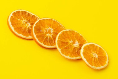 Kurumuş portakal dilimleri parlak sarı bir zemin üzerinde çaprazlama duruyor. Sağlıklı gıda konsepti, vitaminler, aromaterapi ve dekor.