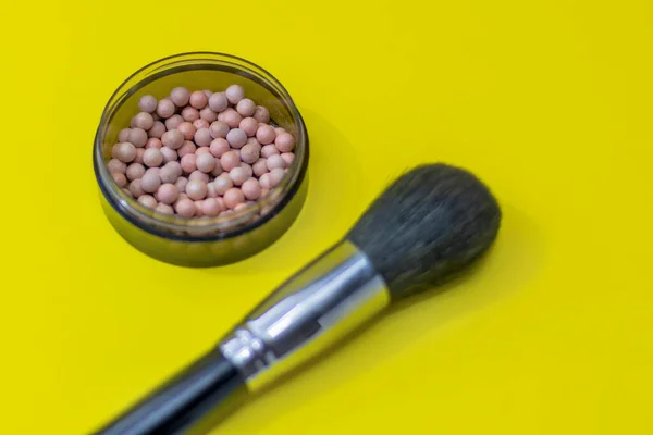 Cosmetic powder balls blush and makeup brush close-up, shallow depth of field. Bright yellow background. Brush is out of focus.