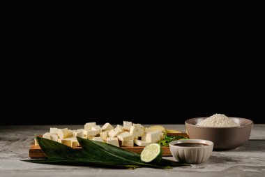Bambu yaprakları üzerinde taze tofu parçaları, soya sosu, pirinç, zencefil ve limon ağacının yanında ahşap bir tahta üzerinde. Siyah bir arkaplanda..