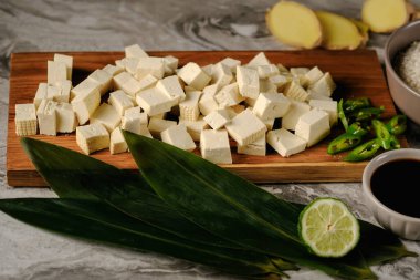 Bambu yaprakları üzerinde taze tofu parçaları, soya sosu, pirinç, zencefil ve limon ağacının yanında ahşap bir tahta üzerinde. Siyah bir arkaplanda..
