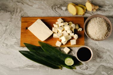 Bambu yaprakları üzerinde taze tofu parçaları, soya sosu, pirinç, zencefil ve limon ağacının yanında ahşap bir tahta üzerinde. Siyah bir arkaplanda..