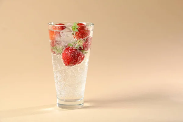 Cocktail glas med röda jordgubbar, mousserande vatten på bubblor på en beige bakgrund — Stockfoto