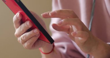 Kızın elleri akıllı telefonun ekranına tıklıyor. Kırmızı telefon, pembe ceket. Evlilik yüzüğü.