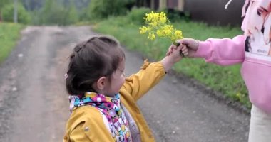 Bir çocuk annesine kır çiçeği verir ve o da karşılık olarak öper.